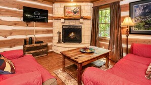 A cozy log cabin interior with a fireplace, a television mounted on the wall, and a scenic painting.