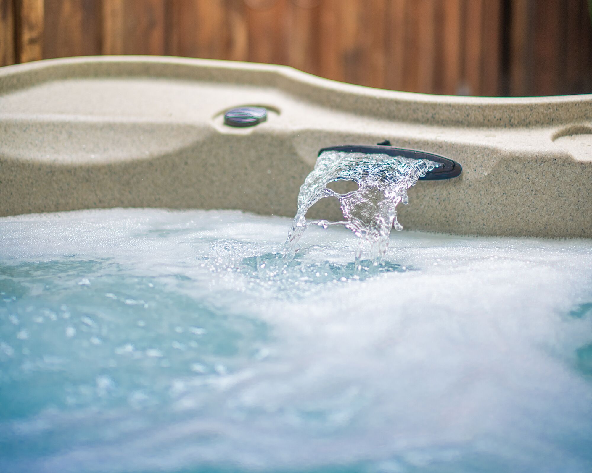 A hot tub with water cascading into it, surrounded by a wooden fence.