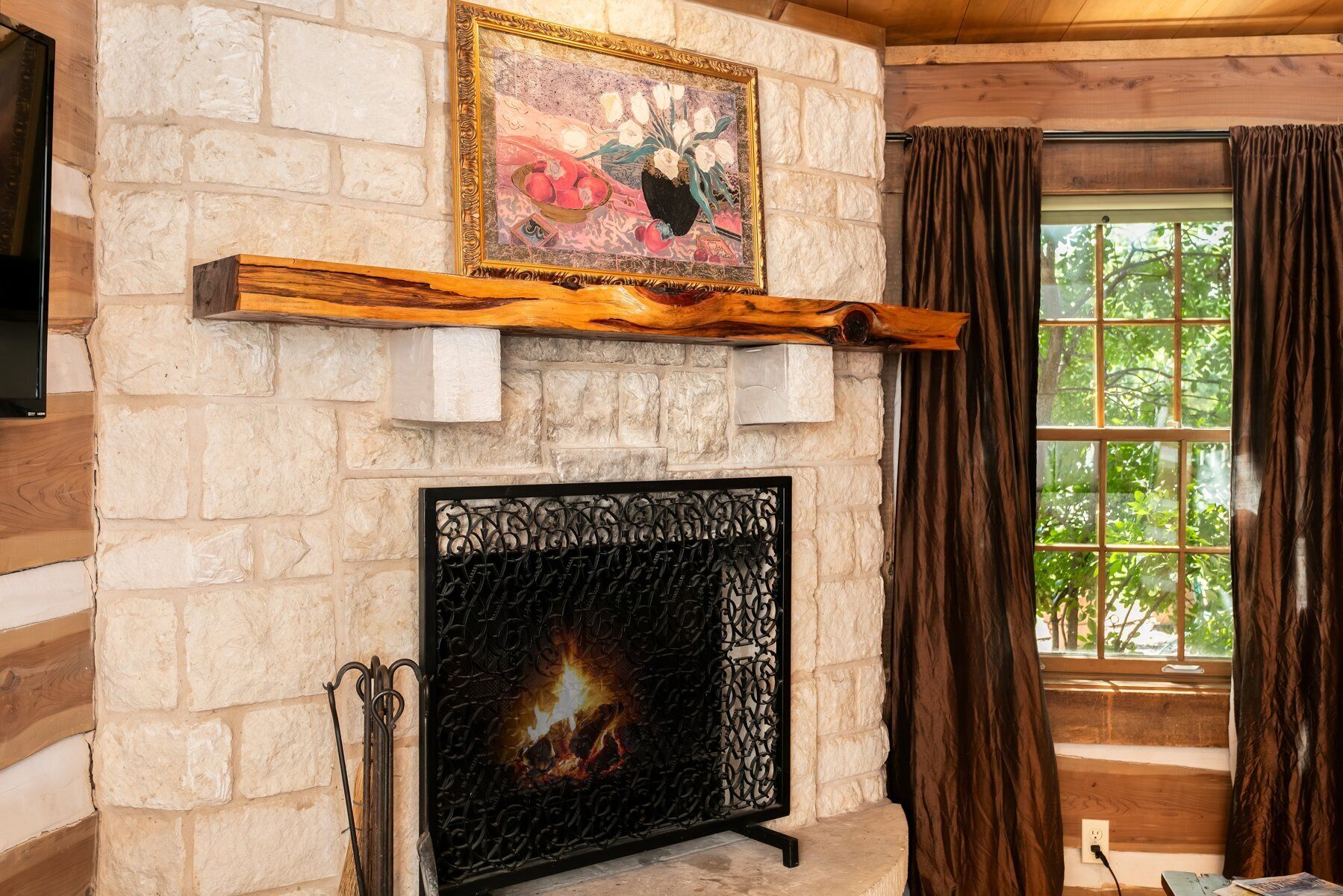 A stone fireplace with a fire, a wooden mantel, and a painting above it.