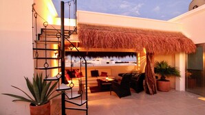 A modern interior with a staircase, a thatched roof, and a seating area with a view of the sky.