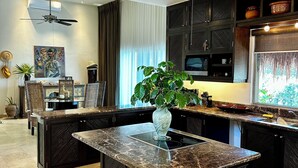 A modern kitchen with a central island, dark cabinetry, and a ceiling fan.