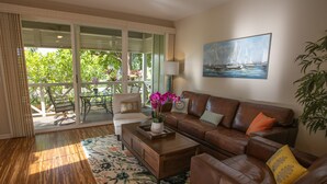 A living room with a brown leather sofa, a coffee table, and a floral rug. There is a painting of a sailboat on the wall and a potted plant on the right.
