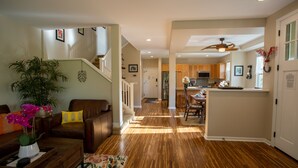 A spacious living room with a wooden floor, a staircase, and a kitchen area in the background.