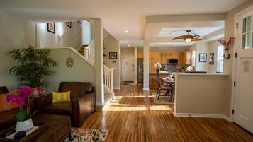 A spacious living room with a wooden floor, a staircase, and a kitchen area in the background.