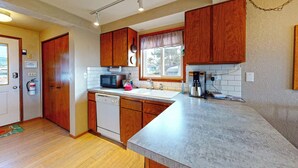 A kitchen with wooden cabinets, a dishwasher, a microwave, a coffee maker, and a window with a view. - OCEAN FRONT: BEACHTOPIA South:  Seaside Vacation Homes, Inc Managed  (Seaside)