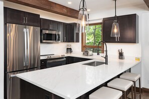 A modern kitchen with stainless steel appliances, a large island with bar stools, and pendant lighting.