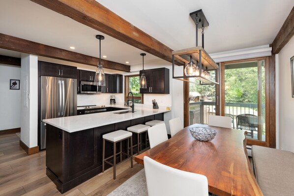 A modern kitchen with a central island, stainless steel appliances, and a dining area with a wooden table and white chairs.