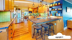 Una cocina con armarios de madera, un refrigerador de acero inoxidable y una isla de madera con taburetes.