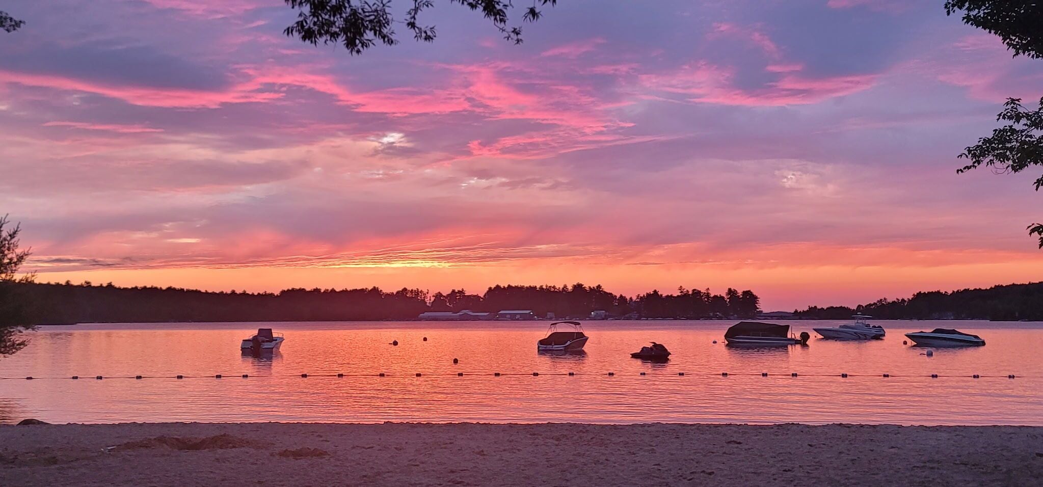 A calm lake with boats anchored in the water, surrounded by trees and a clear sky.