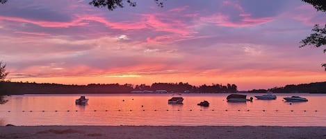 A calm lake with boats anchored in the water, surrounded by trees and a clear sky.