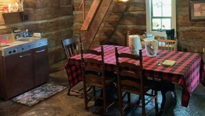 A rustic dining area with a wooden table and chairs, a wooden ceiling, and a window with natural light. - 120Yr Old Cabin Great for couple/family, 15 min from Boone, center of 200 acres! (Boone)