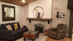 A living room with a dark-colored sofa, a round coffee table, a leather armchair, and a fireplace with a mirror above it. - On the river,Close to Midtown,Fun Trackers, The Inn , Fishing. Sleeps 11 in bed (Ruidoso)