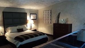 A bedroom with a large bed, a nightstand with a lamp, a dresser, and a glass-enclosed balcony. - On the river,Close to Midtown,Fun Trackers, The Inn , Fishing. Sleeps 11 in bed (Ruidoso)