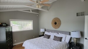 Een slaapkamer met een bed, twee nachtkastjes, een plafondventilator, een raam met jaloezieën en een wanddecoratie.