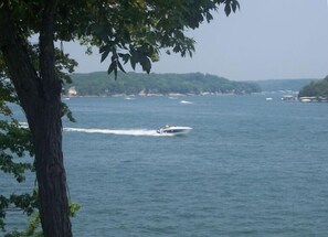 A boat moving across a calm body of water with a tree in the foreground and a distant shoreline with buildings. - NEWLY UPDATED!!!Amazing lakefront home (Gravois Mills)