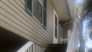 Un escalier avec des rampes blanches menant à une maison aux murs recouverts d’un revêtement beige et aux volets verts.