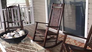 Une véranda abritée avec des fauteuils à bascule en osier, une table en verre et un bol rempli de coquillages.