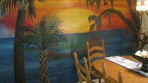 Une pièce comprenant une table à manger, des chaises et un tableau représentant un coucher de soleil sur l’eau.
