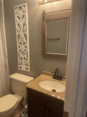 Un baño con inodoro, lavamanos, espejo y un panel decorativo.