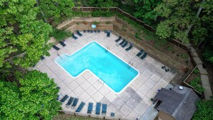 An aerial view of a rectangular swimming pool surrounded by a wooden deck with lounge chairs.