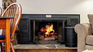 A fireplace with burning logs, a wooden chair, and a black trash can.