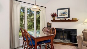 A dining area with a table and chairs, a fireplace, and a view of the outdoors.