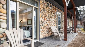 A stone exterior with wooden beams, a covered porch with Adirondack chairs, and a visible interior with a sofa and a lamp. - Mountain View Chalet - Large Outdoor Pool and Hot tub - Pet Friendly (Canmore)