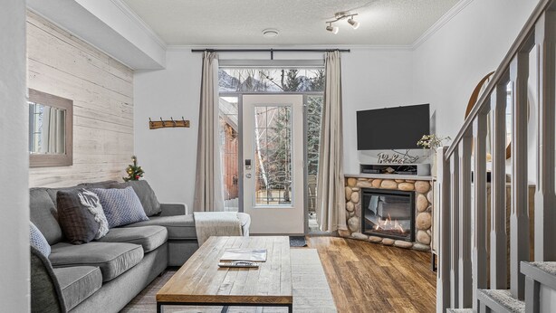 A living room with a gray sofa, a coffee table, a fireplace, and a TV mounted on the wall. - Mountain View Chalet - Large Outdoor Pool and Hot tub - Pet Friendly (Canmore)
