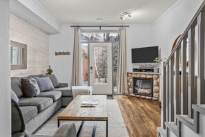 Ein Wohnzimmer mit grauem Sofa, Couchtisch, Kamin und Wandfernseher.