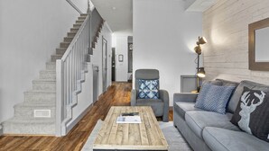 A modern living room with a staircase, grey sofa, and a coffee table. - Mountain View Chalet - Large Outdoor Pool and Hot tub - Pet Friendly (Canmore)