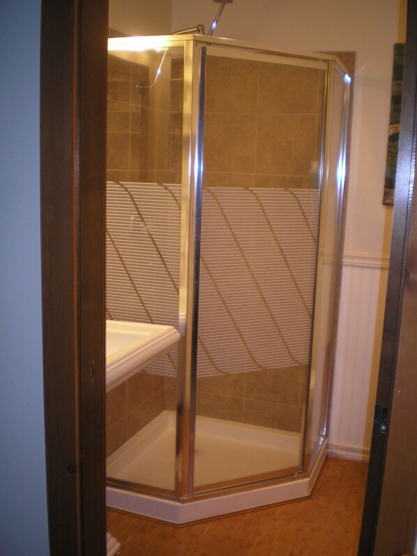 A glass-enclosed shower stall with a white shower seat and a tiled wall.