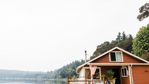 Une cabane en bois dotée d’une terrasse, d’un petit porche et offrant une vue sur un lac.