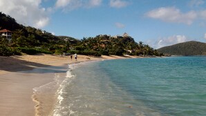 Una playa con aguas cristalinas, una orilla arenosa y edificios en una colina.