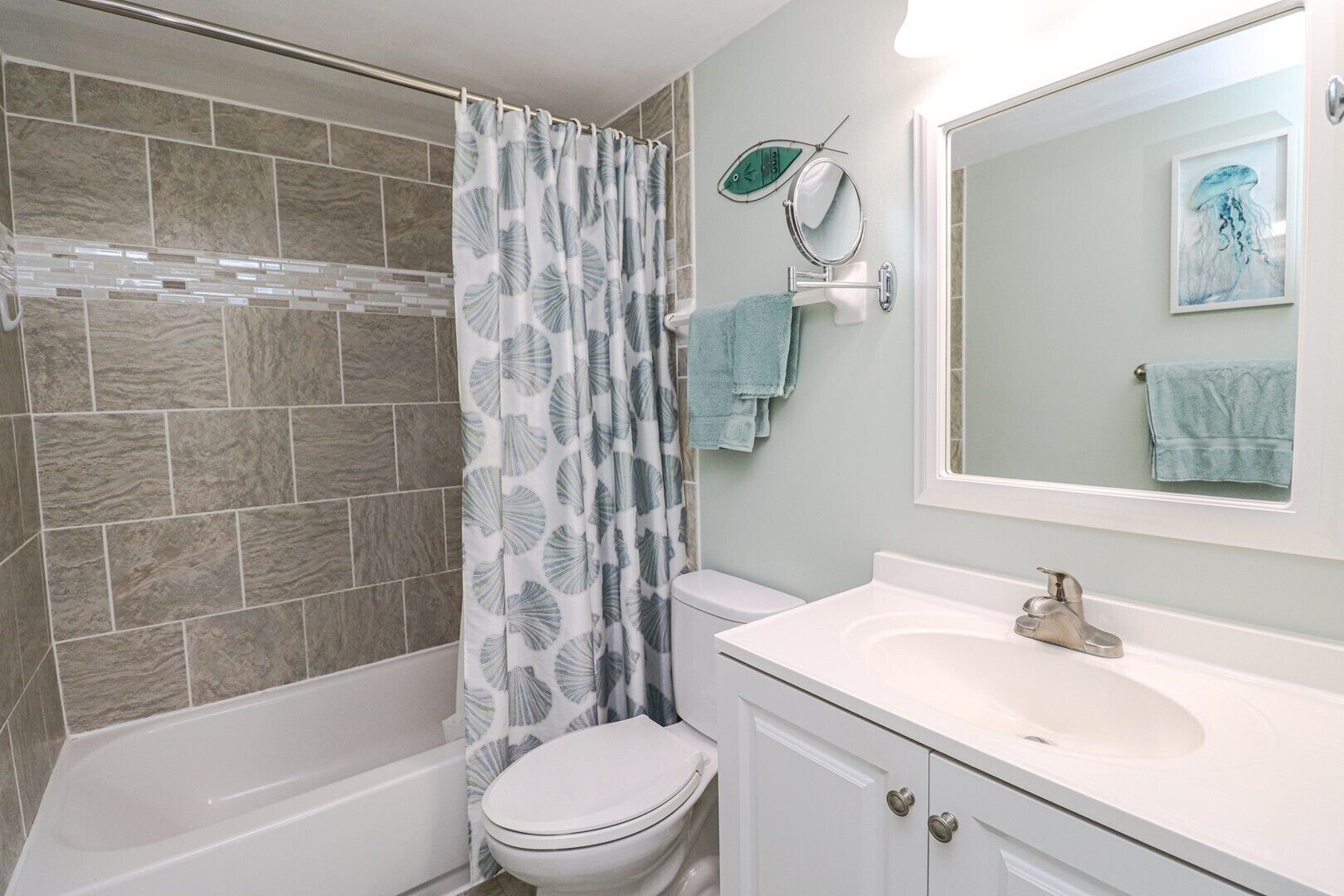A bathroom with a shower, toilet, sink, and a mirror with a framed picture.