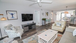 Un salon moderne doté d’un téléviseur à écran plat, d’un ventilateur de plafond et d’un coin repas avec des chaises et une table.