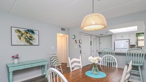 Un espace repas comprenant une table en bois, des chaises blanches, un banc de couleur turquoise et un luminaire suspendu.