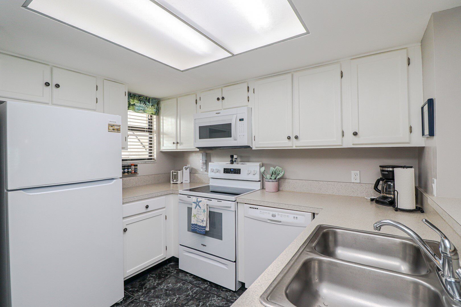 A compact kitchen with white cabinets, a microwave, a stove, a dishwasher, and a sink.