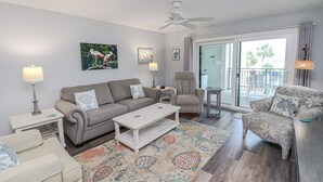 Un salon comprenant un canapé, un fauteuil, une table basse et donnant sur le balcon extérieur.