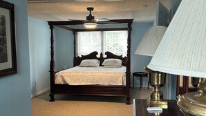 Une chambre à coucher avec un lit à baldaquin, un ventilateur de plafond, une lampe et une fenêtre avec des stores.