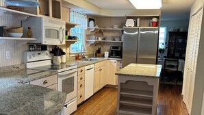 Une cuisine moderne avec des meubles blancs, des plans de travail en granit, un réfrigérateur en acier inoxydable et un four encastré.