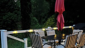 Une terrasse dotée d’une table ronde et de chaises, entourée d’une rambarde agrémentée de guirlandes lumineuses.