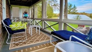 A covered porch with two chairs and a table, a lattice fence, and a view of a green landscape. - Barn at Blue Hill Peninsula Historic farm w/Organic Meadows. Pet friendly (Brooksville)