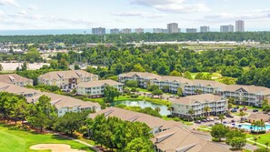 A residential complex with multiple apartment buildings, a swimming pool, and a golf course in the background. - Luxury Golf-View Condo • Barefoot Resort • Resort Pools • Premium Beach Gear (North Myrtle Beach)