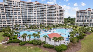Um hotel grande com várias varandas e uma piscina central rodeada por palmeiras e espreguiçadeiras.