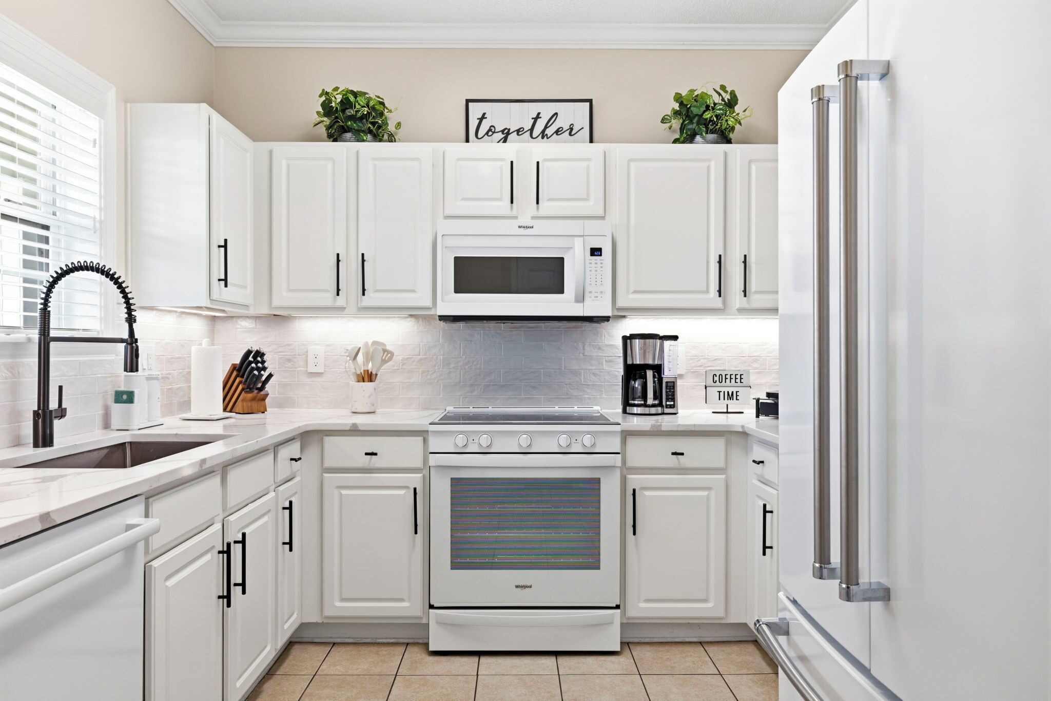A modern kitchen with white cabinetry, a built-in microwave, a stainless steel refrigerator, and a coffee maker.