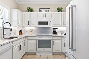 A modern kitchen with white cabinetry, a built-in microwave, a stainless steel refrigerator, and a coffee maker. - Luxury Golf-View Condo • Barefoot Resort • Resort Pools • Premium Beach Gear (North Myrtle Beach)