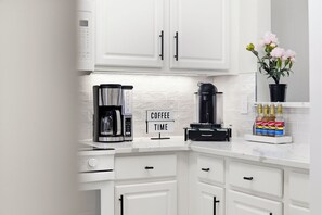 Une cuisine moderne avec des meubles blancs, une machine à café, une machine Nespresso et un panneau indiquant « PAUSE CAFÉ ».