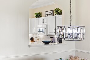 A kitchen with white cabinets, a microwave, a black bowl, and a hanging light fixture.