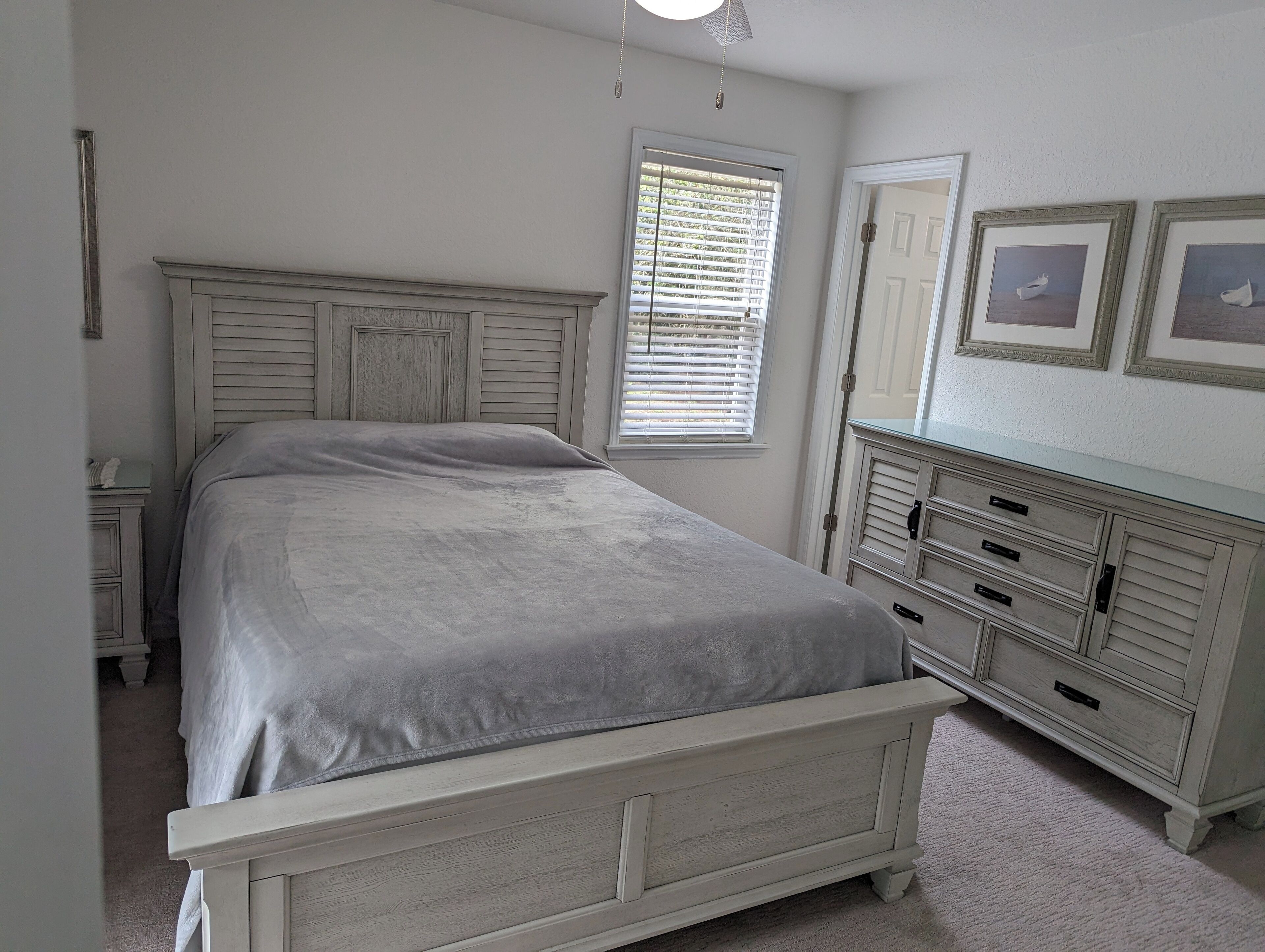 A bedroom with a bed, a dresser, a nightstand, and a window with blinds.