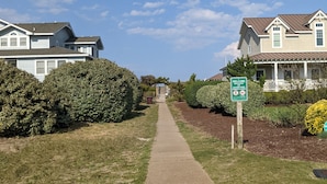 Un chemin mène à une rangée de maisons, agrémentée d’une pancarte « Bienvenue », et bordé de pelouses et de haies bien entretenues.